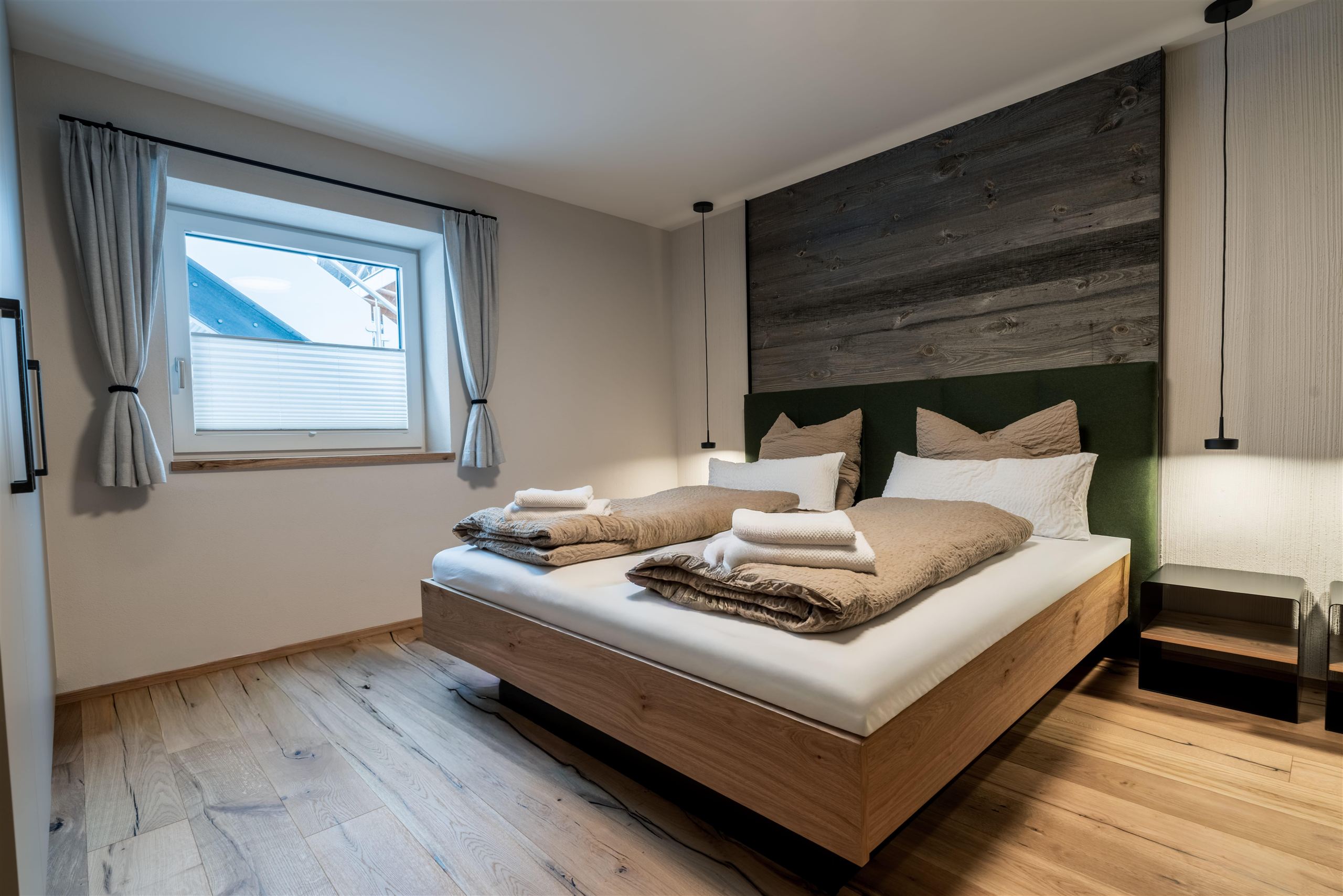 A modernly furnished room with a television on the wall and a large mirror. Bright, inviting light can be seen through the window.