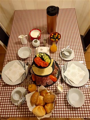 Ein schön gedeckter Tisch mit verschiedenen Speisen, einschließlich Wurst, Käse und frischem Brot. Dazu gibt es Getränke und eine Schüssel mit bunten Süßigkeiten.