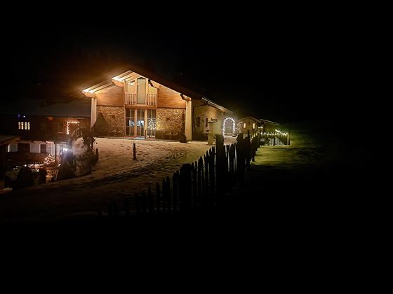 Das Almchalet Riederhäusl in der Nacht, beleuchtet von warmem Licht. Es liegt in einer verschneiten Umgebung mit einer einladenden Atmosphäre.