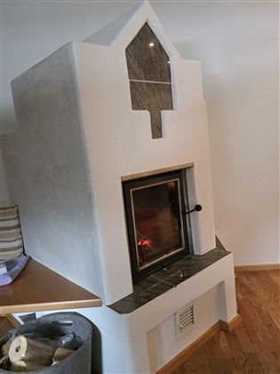 Een moderne haard met een strak, wit ontwerp en een verwarmd oppervlak. Naast de haard ligt hout voor het volgende gebruik.