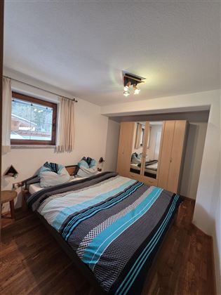 Ein gemütliches Schlafzimmer mit einem Doppelbett und Holzfußboden. Der Raum hat einen großen Schrank und Fenster mit Aussicht.