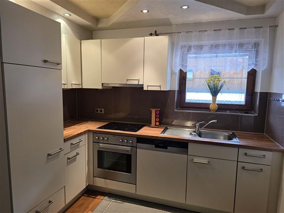 Een moderne keuken met lichte kasten en een houten werkblad. Het raam biedt uitzicht naar buiten en een klein groen plantenaccent.