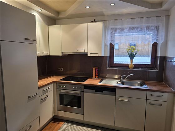 Een moderne keuken met lichte kasten en een houten werkblad. Het raam laat veel licht binnen en toont een plant op de vensterbank.