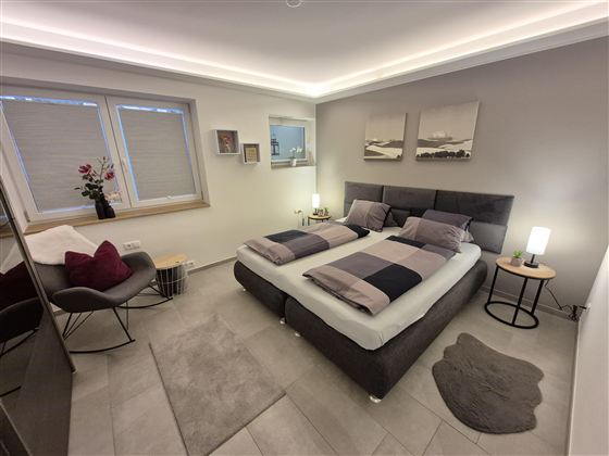 Ein modernes Schlafzimmer mit einem Doppelbett und stilvollen Kissen. Sanfte Beleuchtung und minimalistische Dekoration schaffen eine einladende Atmosphäre.