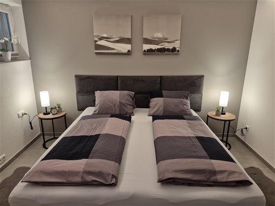 Ein modernes Schlafzimmer mit zwei getrennten Betten. Die Wände sind hell, und es gibt Nachttische mit Lampen.