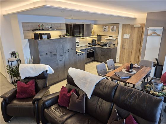 Eine moderne Ferienwohnung mit einer offenen Küche und einem gemütlichen Wohnbereich. Der Raum ist hell und einladend, mit einem Esstisch und bequemen Sofas.