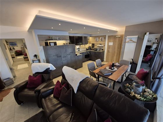 Eine moderne Wohnung mit einer offenen Küche und einem gemütlichen Wohnbereich. Der Essplatz ist in einem einladenden Raum mit komfortablen Möbeln eingerichtet.