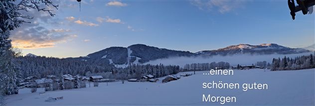 Een besneeuwd berglandschap met hutten op de voorgrond. De lucht is helder en er straalt een zachte ochtendlicht.