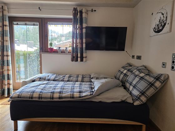 Een gezellige slaapkamer met twee eenpersoonsbedden en een tv aan de muur. De ramen hebben gordijnen en bieden uitzicht op een groene landschap.