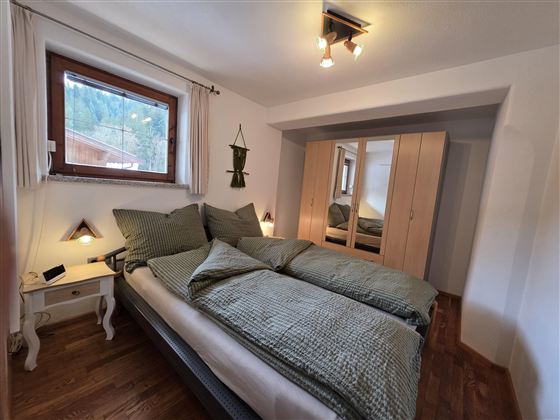 Een gezellig slaapkamer met twee eenpersoonsbedden en groene dekens. Grote ramen laten veel daglicht binnen en de ruimte is eenvoudig en elegant ingericht.