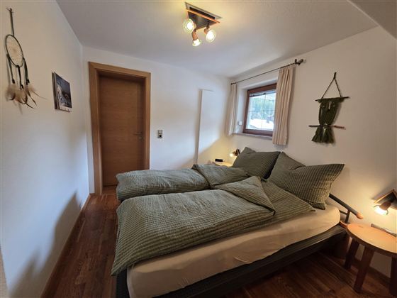 Een gezellige slaapkamer met een tweepersoonsbed en groen gestreepte dekens. De muren zijn licht en de inrichting is eenvoudig en uitnodigend.