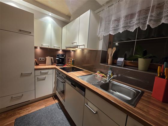 Een moderne keuken met lichte kasten en houten werkbladen. De uitrusting omvat een kraan, een gootsteen en een kleine eettafel.