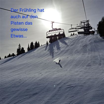 Een met sneeuw bedekte piste in de lente met een skiër. Op de achtergrond zijn skiliften en een heldere lucht te zien.