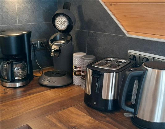 A modern kitchen corner with a coffee machine, a kettle, and a toaster. The wooden countertop gives the scene a cozy atmosphere.
