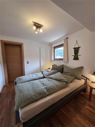 Ein gemütliches Schlafzimmer mit zwei Einzelbetten und Holzboden. Die Wände sind hell gestrichen und ein Fenster sorgt für Tageslicht.