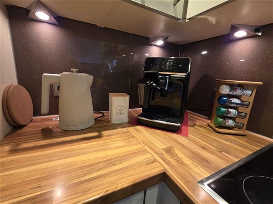 Eine moderne Küche mit einem Holzarbeitsplatz. Auf der Theke stehen eine Kaffeemaschine, ein Wasserkocher und ein Gewürzregal.