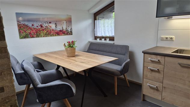 A cozy dining area with a wooden table and modern chairs. On the wall, there is a picture of a beautiful landscape with flowers.