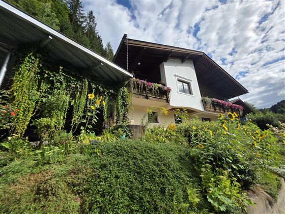 Een charmant huis omringd door weelderig groen en kleurrijke bloemen. De lucht is gedeeltelijk bewolkt en geeft de scène een aangename sfeer.