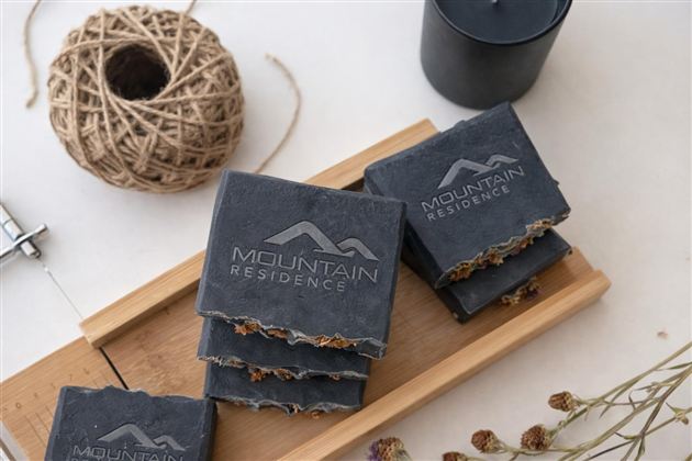 Ein stilvolles Arrangement von Seifen auf einem Holzbrett. Die Seifen sind mit dem Logo "Mountain Residence" graviert und umgeben von dekorativen Elementen wie Schnur und Kerze.