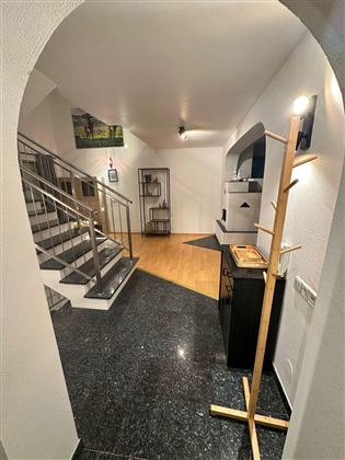 Ein einladender Eingangsbereich mit einer Treppe und modernen Möbeln. Der Boden ist aus schwarzem Marmor und es gibt ausreichende Beleuchtung.