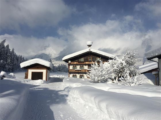 Ein malerisches Haus in einer verschneiten Landschaft. Hoher Schnee bedeckt den Boden und die Bäume unter einem klaren Himmel.