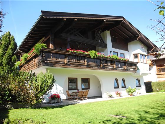 Ein schönes, traditionelles Haus mit einem Balkon voller Blumen. Darum herum gibt es einen gepflegten Garten mit grüner Rasenfläche.