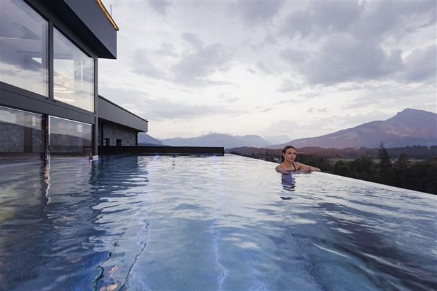 Een modern infinitypool met uitzicht op bergen en een bewolkte lucht. Een persoon ontspant in het water.
