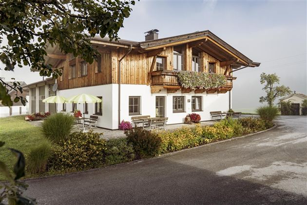 A charming house in alpine style with wooden cladding and a balcony. Surrounded by green meadows and blooming plants.