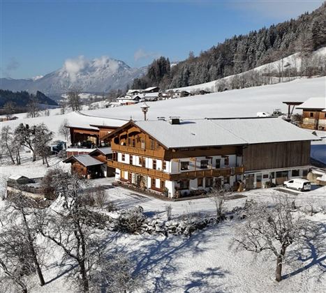 Ein malerisches Chalet im Schnee mit Bäumen und Bergen im Hintergrund. Die Landschaft ist ruhig und winterlich.