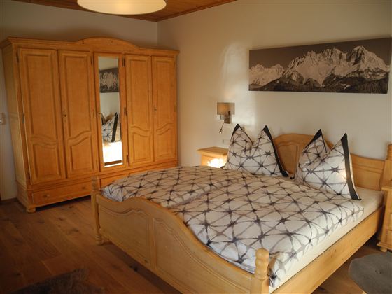 Ein gemütliches Schlafzimmer mit einem großen Bett und traditionellen Holzmöbeln. Der Raum hat eine warme Atmosphäre und eine schöne Berglandschaft an der Wand.