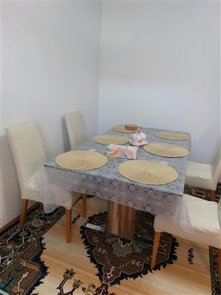 Ein Essbereich mit einem Holzstammtisch und weißen Stühlen. Der Tisch ist mit einer Tischdecke und Untersetzer dekoriert.