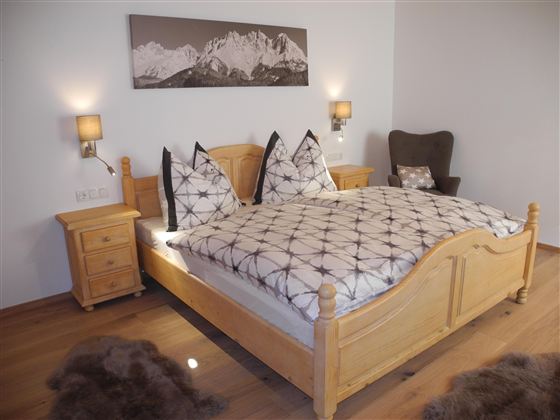 Ein gemütliches Schlafzimmer mit einem großen Holzbett und dekorativen Kissen. An den Wänden hängen Bilder und es gibt Nachttische neben dem Bett.