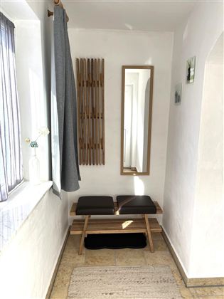 Ein heller Eingangsbereich mit einer Holzbank und einem großen Spiegel. An der Wand hängt ein Handtuchhalter und ein grauer Vorhang ist zu sehen.