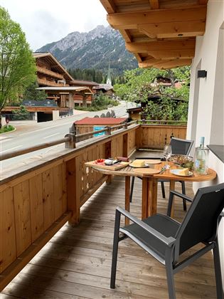 Ein gemütlicher Balkon mit Holzmöbeln und Blick auf die Berge. Auf dem Tisch stehen Snacks und Getränke.