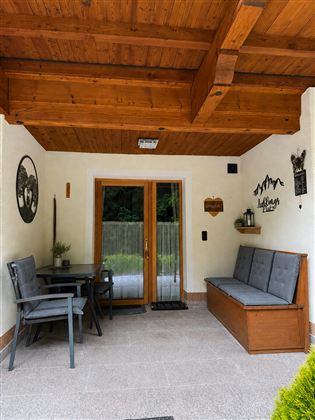 A cozy terrace with wooden beams and a large window. There is a table with chairs and a wooden bench.