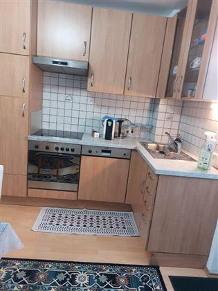 Eine moderne Küche mit Holzschränken und einem hellen Farbschema. Sie ist gut eingerichtet mit Herd, Spüle und verschiedenen Küchenutensilien.