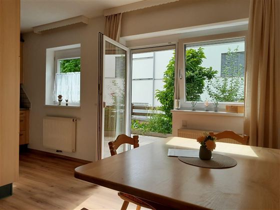 Das großzügige Wohn- und Esszimmer überzeugt mit viel Tageslicht, einer gemütlichen Atmosphäre und direktem Zugang zur Terrasse. Der Essbereich lädt zu gemeinsamen Mahlzeiten ein, während die großen Fenster einen schönen Blick ins Grüne bieten – der ideale Ort zum Entspannen und Wohlfühlen.