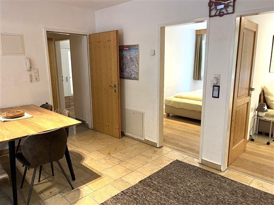 Ein heller und einladender Eingangsbereich mit einem Tisch und Stühlen. Im Hintergrund sind Türen zu weiteren Räumen sichtbar.