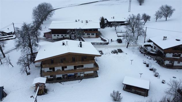 A wintry landscape with several houses covered in snow. The sky is gray and the surroundings appear calm and peaceful.