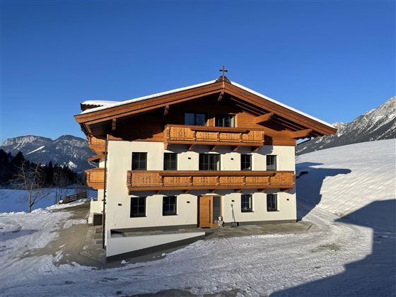 A modern chalet in alpine style, surrounded by snow. The clear blue sky complements the picturesque landscape.