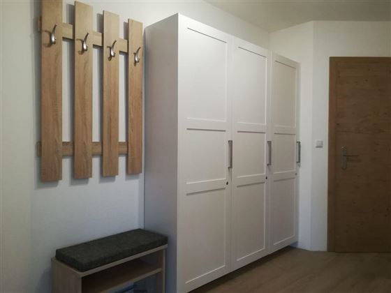 A modern hallway with a white closet and a bench. Wooden coat hooks are hanging on the wall.