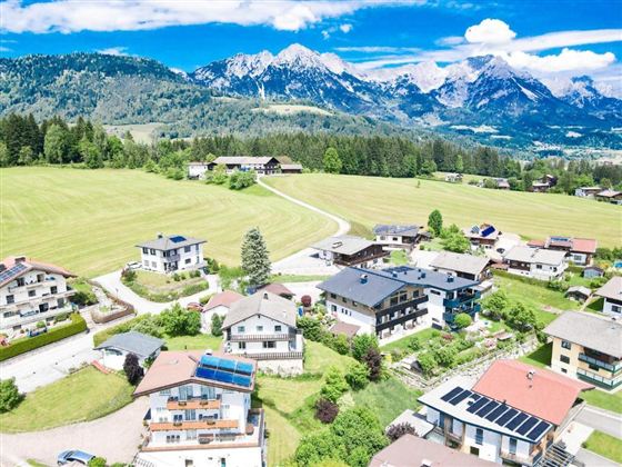A picturesque landscape with houses in a green valley. Majestic mountains rise in the background under a clear blue sky.