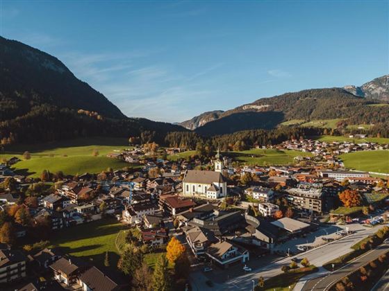 A picturesque view of a small village surrounded by mountains and green meadows. In the center stands a church, surrounded by traditional houses and colorful trees.