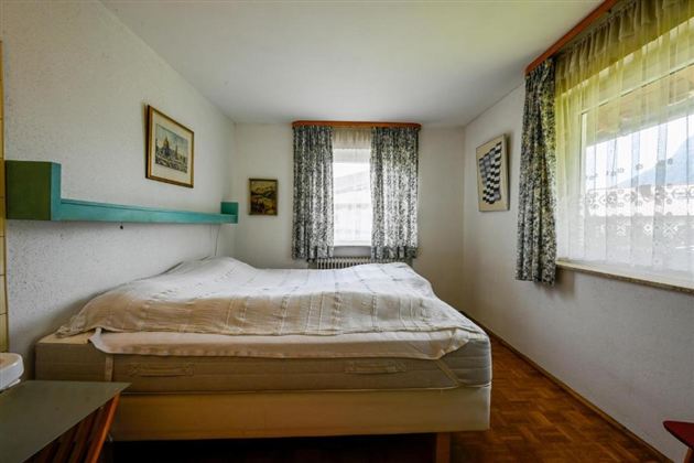 A simple bedroom with a large bed and wooden floor. Curtains and pictures on the walls create a cozy atmosphere.
