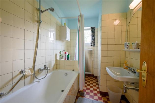 A simple bathroom with a bathtub and a hand washbasin. The walls are tiled and there is a small window for ventilation.