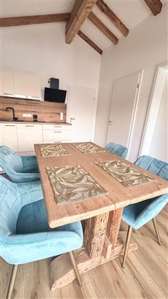 Een uitnodigende eetruimte met een rustieke houten tafel en blauwe stoelen. De moderne keuken op de achtergrond aanvult het eenvoudige, lichte ontwerp.