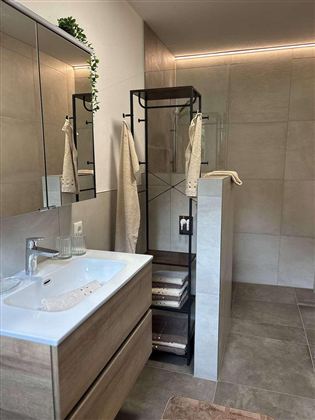 Ein modernes Badezimmer mit einer stilvollen Dusche und einem Holzwaschbecken. Die Wände sind in neutralen Tönen gehalten, wodurch der Raum hell und einladend wirkt.