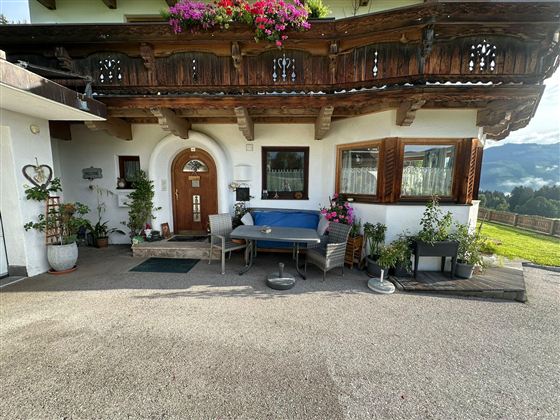 Ein gemütliches Haus mit einem schönen Balkon voller Blumen. Vor dem Eingang stehen Pflanzen und Gartenmöbel.