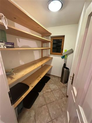 Ein kleiner Raum mit hölzernen Regalen an der Wand. Der Raum hat einen Fensterblick und einen Abfalleimer in der Ecke.