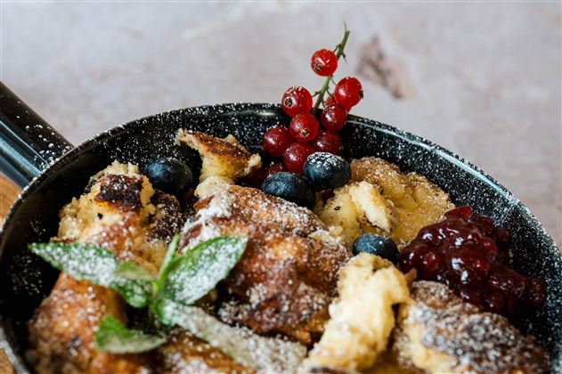 Eine appetitliche Pfanne mit gebackenem Brot, garniert mit Beeren und einem Hauch von Puderzucker. Frische Minze und rote Johannisbeeren ergänzen das Gericht.